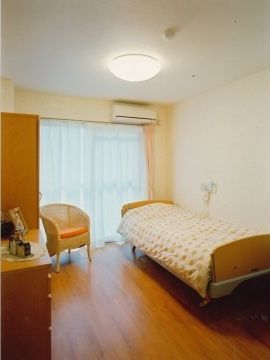 居室には大きなガラス引き戸があり、床はフローリングになっている。ベッド、ナースコール、椅子、収納家具が設けられている。