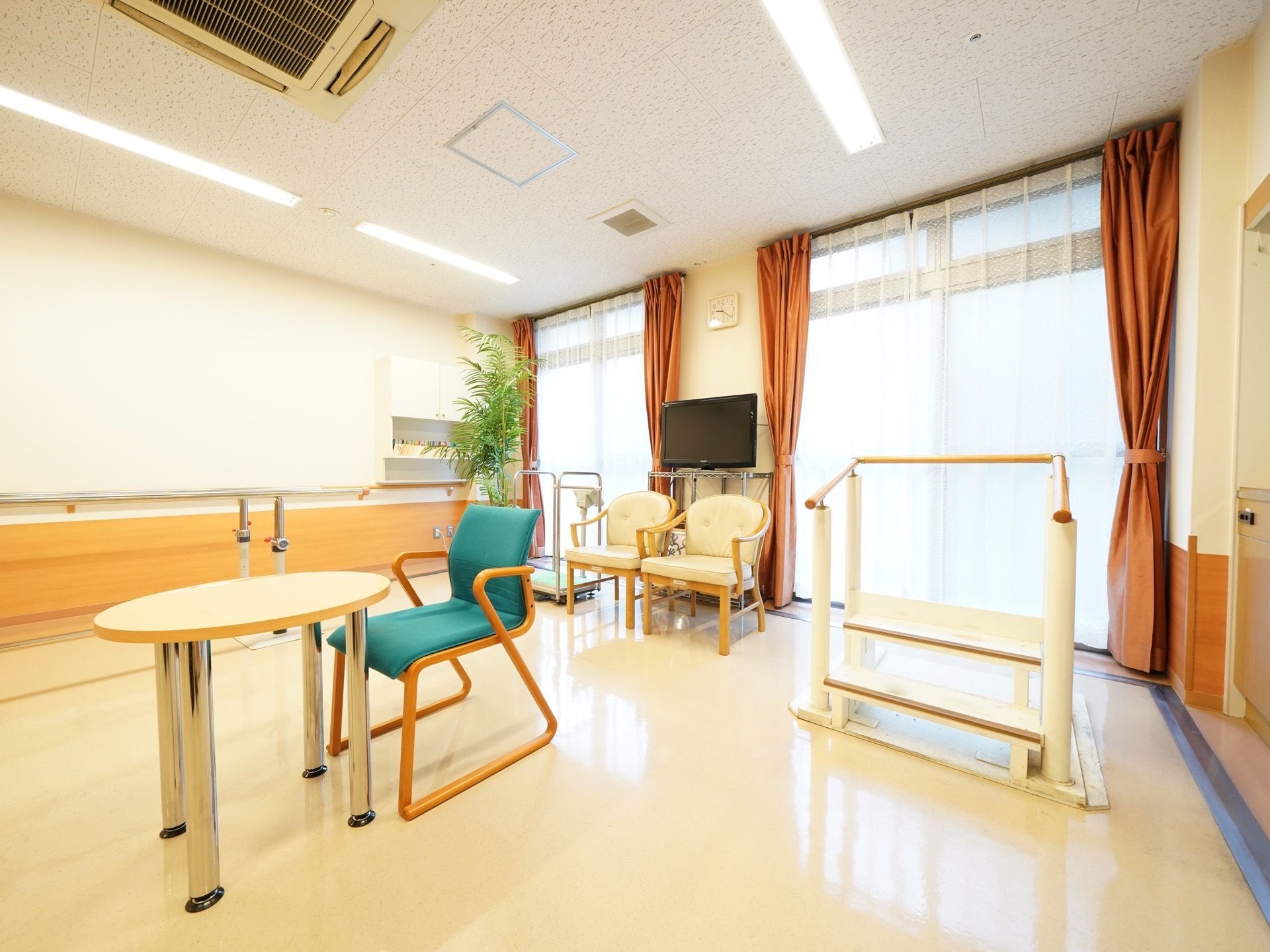 歩行や昇降などのリハビリを行えるリハビリルーム。入居者様のペースでリハビリを行えるようテレビや休憩が行えるスペースも用意している。
