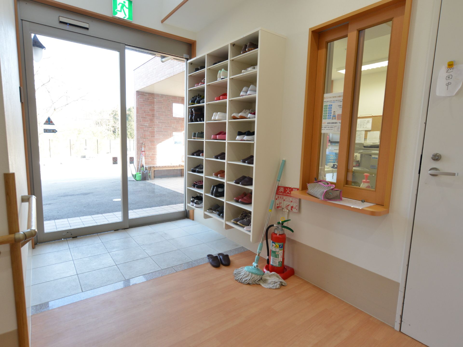 玄関の内側の片面の壁に靴箱が設置されており、その並びに受付カウンターがある。下に消火栓がセットしてある。