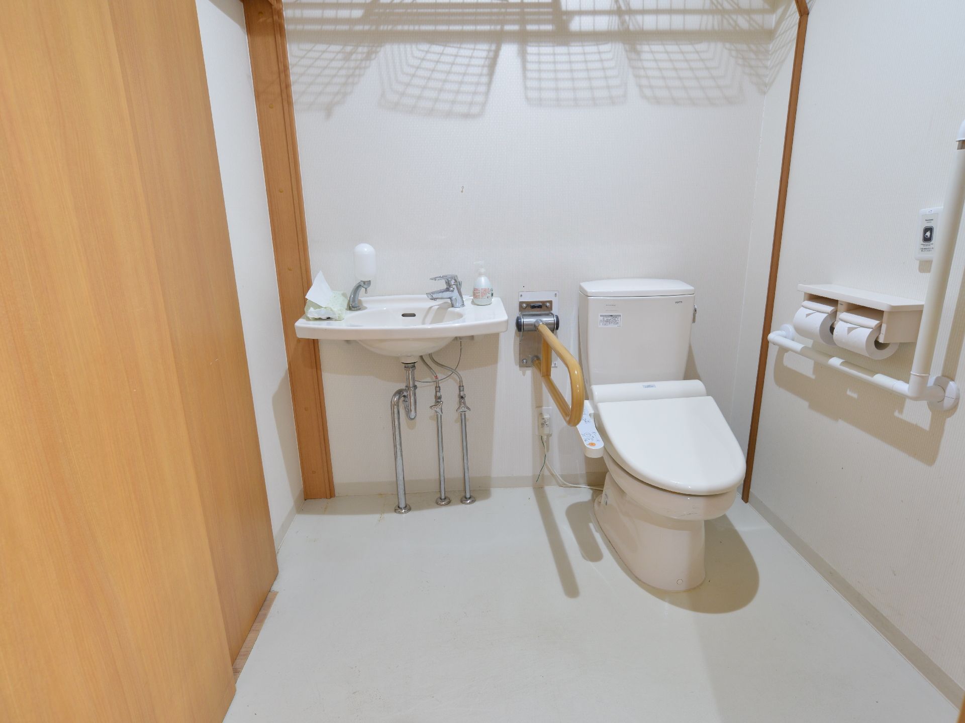 広めのスペースのトイレは洋式で、ウォシュレットが付いている。すぐ横に洗面台、手すり、呼び出しボタンが設置されている。