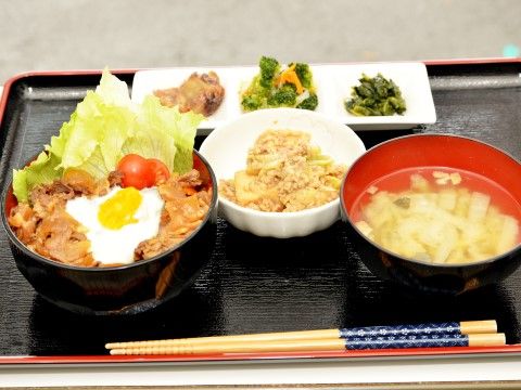 黒のトレイに丼物をメインとした食事と、汁物、小鉢が用意されている。肉類やお漬物があり、偏らないような工夫がなされている。 タイトル 食事