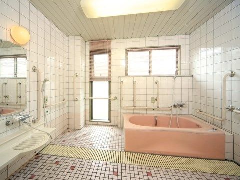 浴室の壁には、手すりが多く取り付けられ、入居者様が安全に入浴できるよう配慮されている。シャワーと浴槽がある。