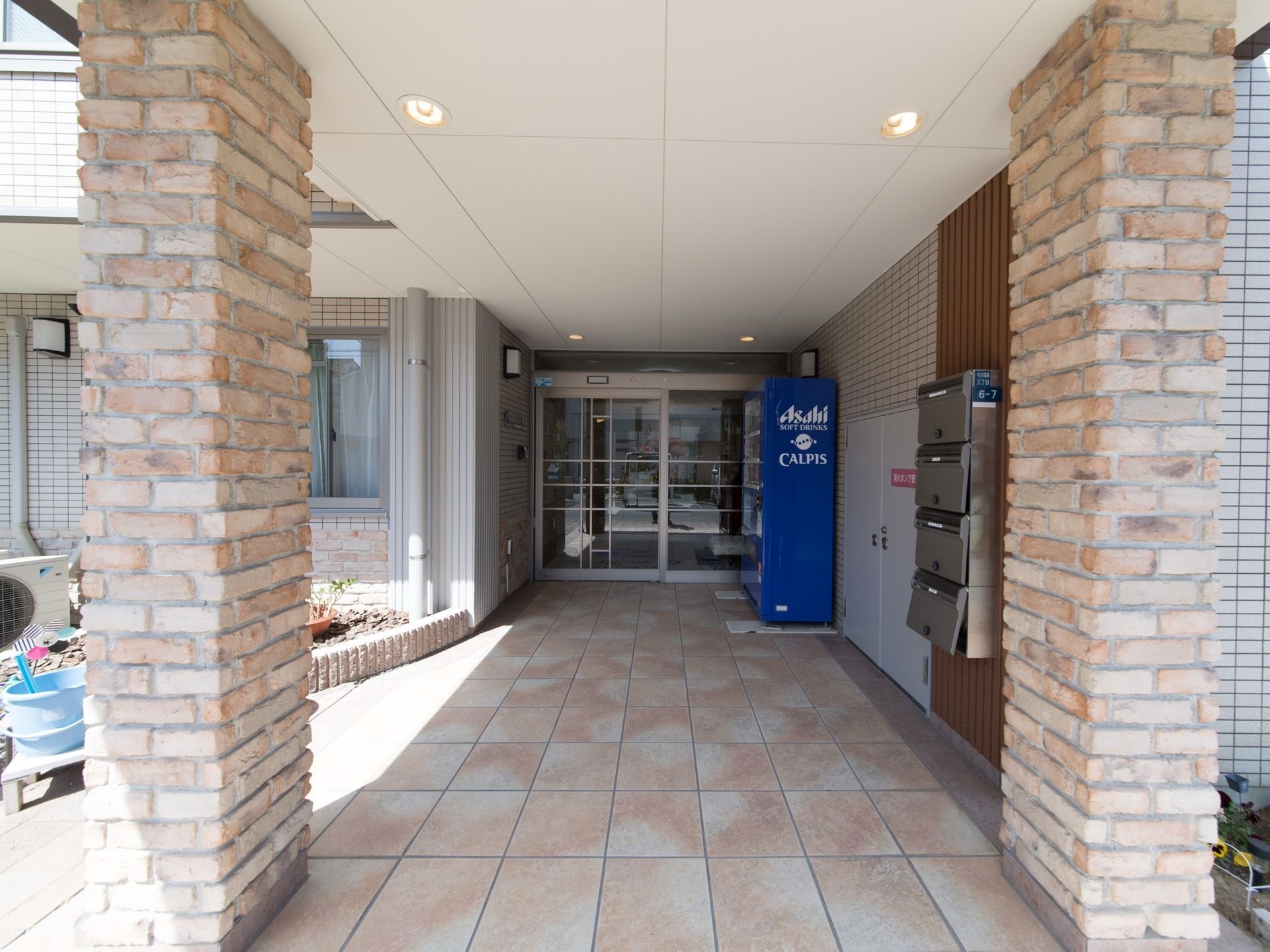 広々とした屋根付きの玄関前スペースである。ガラス張りの出入口ドアを採用し、横の壁際に自動販売機を備えている。