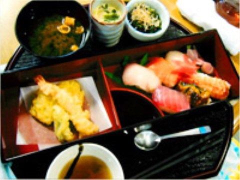 黒い円形のトレイに並べられた、天ぷらやお寿司の定食
