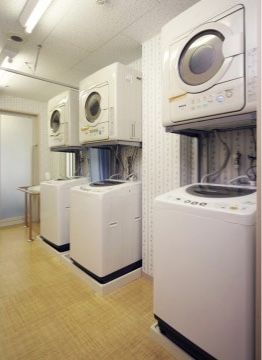 クッションフロア張りの洗濯室には、曇りガラスの扉がある。洗濯機の上に乾燥機がのっており、合計３セット用意している。