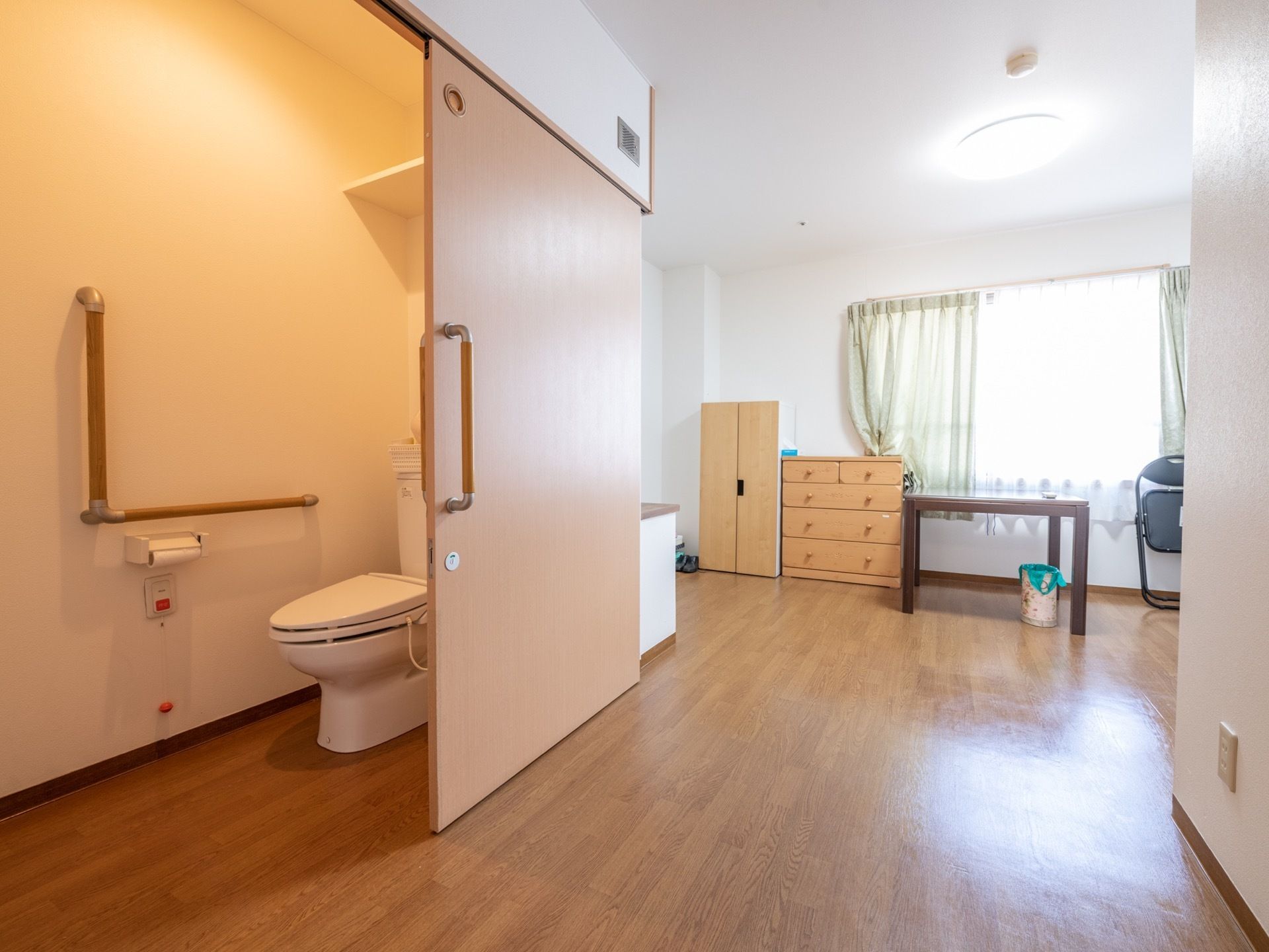 居室内は広々としていてトイレが設置されており、引き戸が開いている。フローリングの床は全てフラットになっている。