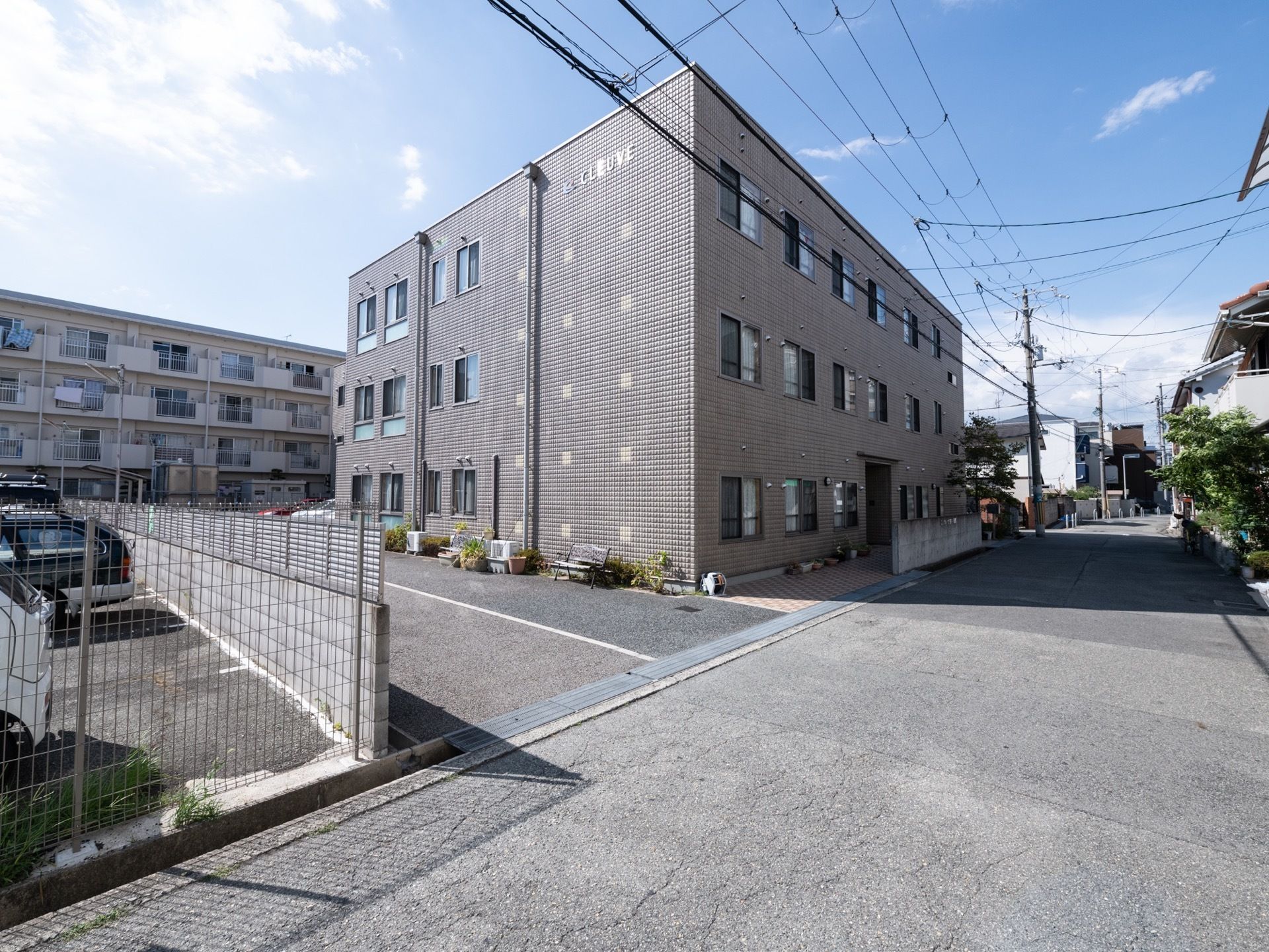 建物の横には広々としたコンクリートのスペースがある。壁際に木製のベンチや植物の鉢植えなどが置かれている。