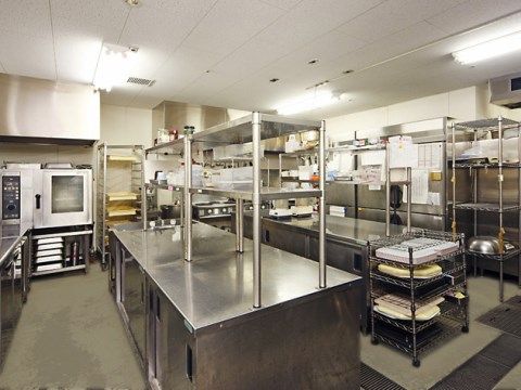 中央に作業台が２列に並んでいる。壁際には冷蔵庫やガス台などがある。収納や配膳台などもステンレス製で、輝いている。