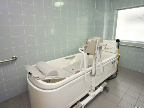 床と壁がタイル貼りで窓がある。特殊介助浴槽とその脇には横になったまま浴槽に入る電動リフトが置いてある。