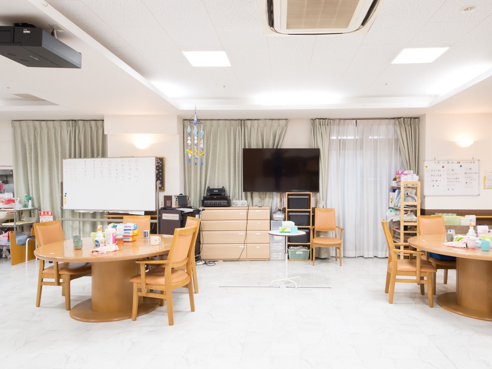 窓にはカーテンが閉められ、窓際にはテレビやホワイトボードが置いてある。長細い丸テーブルの上には、さまざまなものが置いてある。