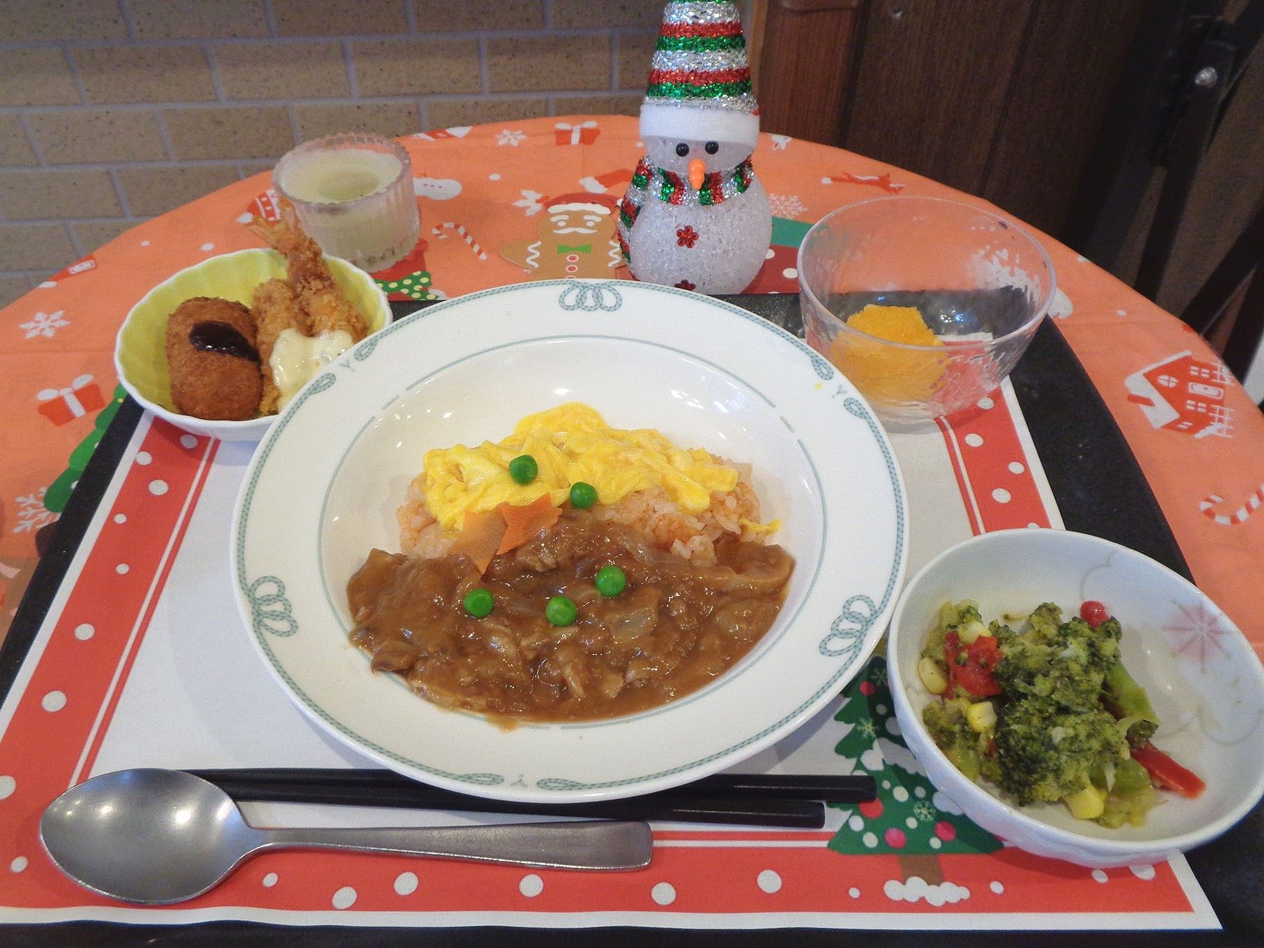 トレーの上にご飯、シチュー、沢庵、和え物、ミカンが置いてある。お箸とともにスプーンが２つ用意されている。