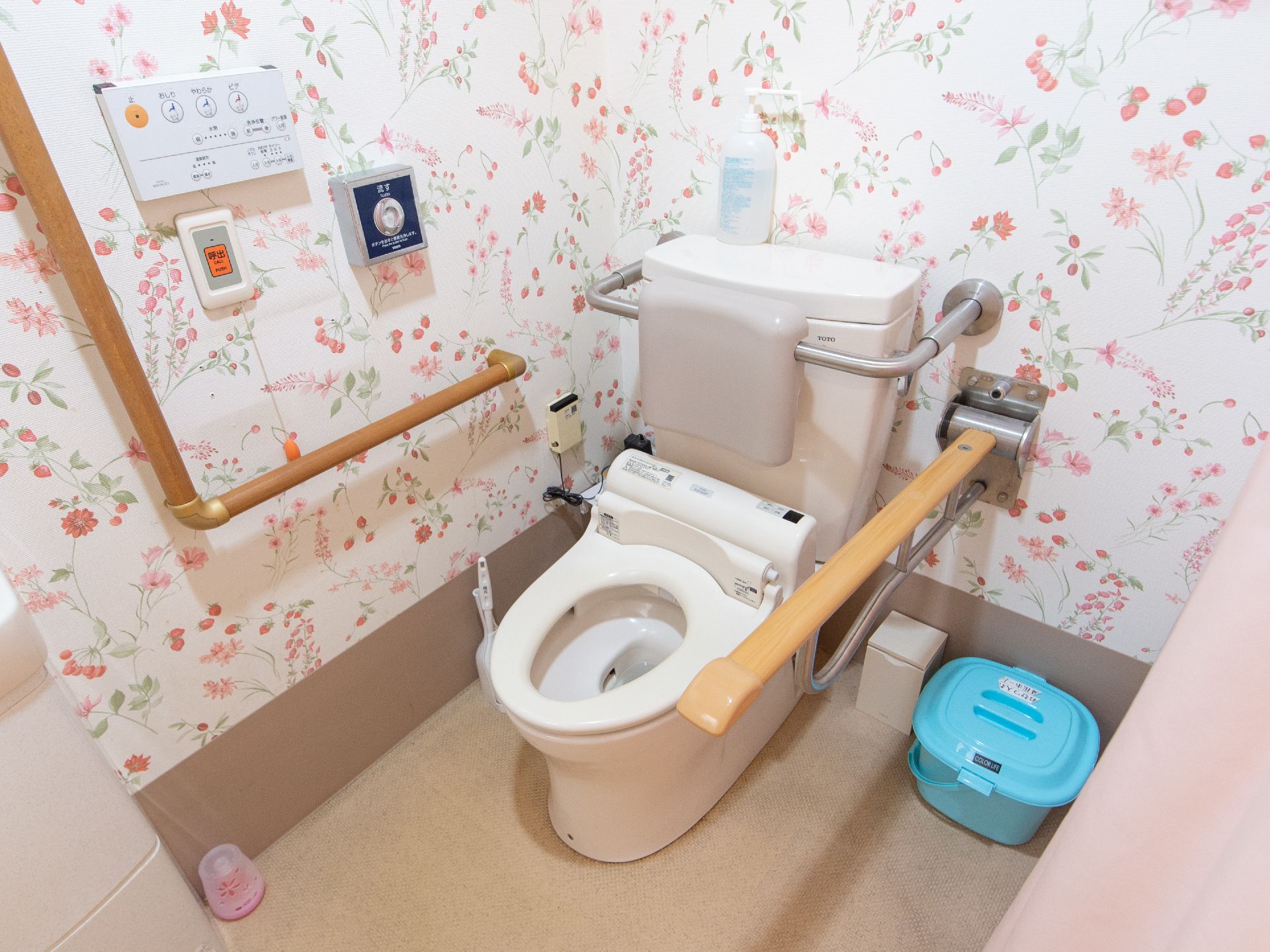 華やかな雰囲気のトイレには、温水洗浄便座が完備されており、背もたれパッドや可動式手すりが設置されている。