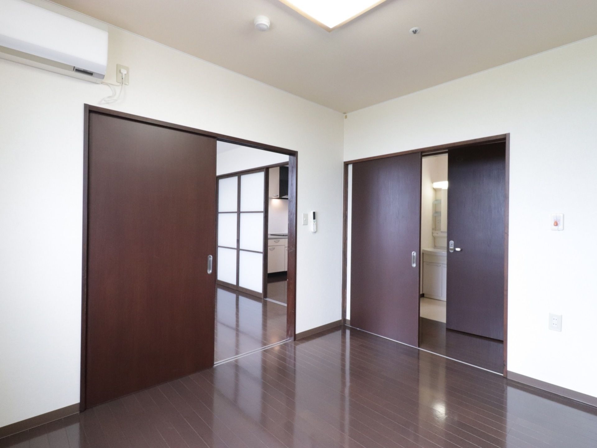 ドアで区切られた部屋が２つあり、奥にはキッチンと洗面台が見える。室内のドアはスライド式のものが使用されている。