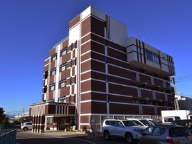 5階建ての建物には、茶色に白いラインが入っている。周囲に高い建物がなく、開放的。エントランスの上には屋根が張り出している。