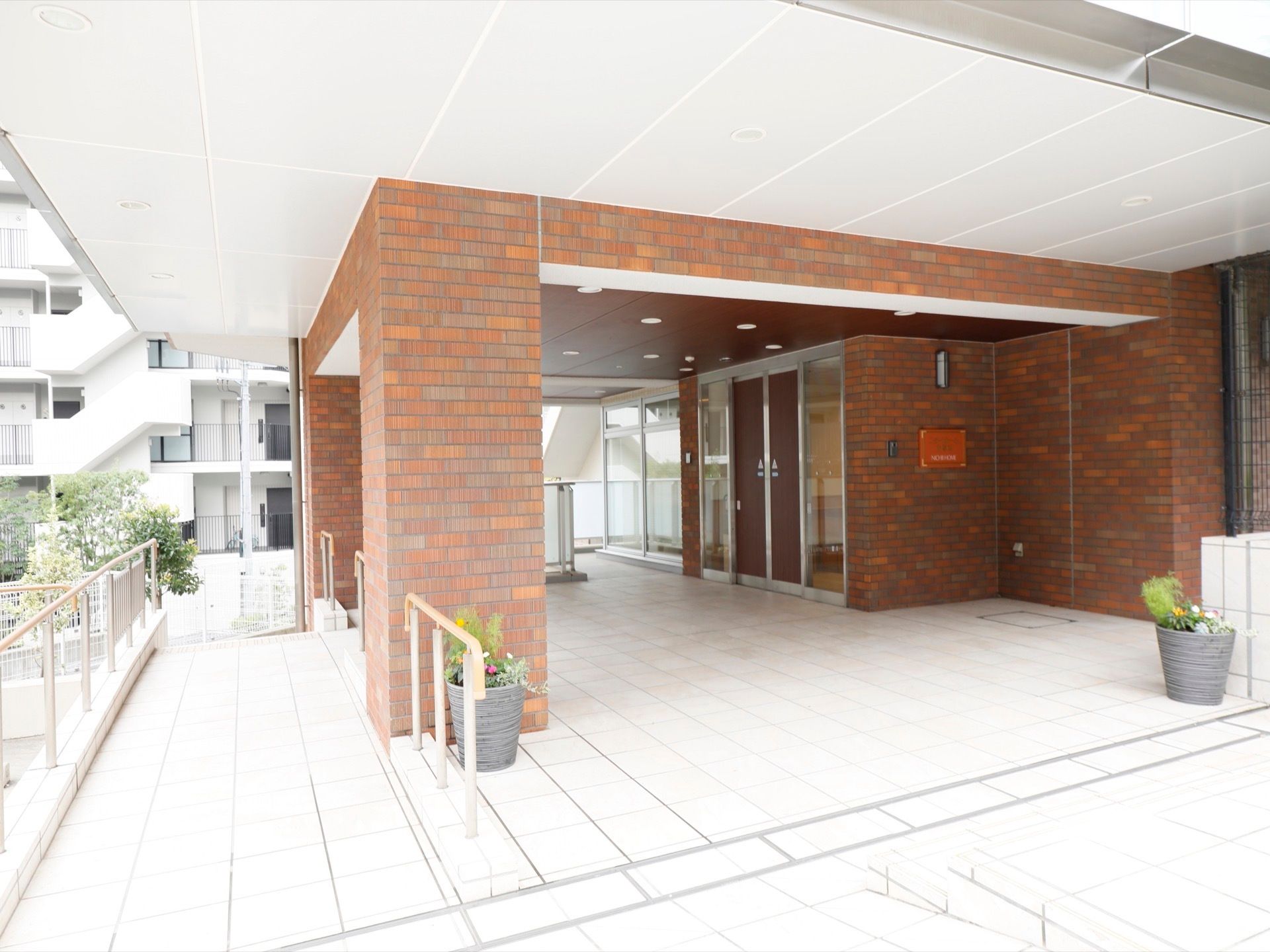 レンガ調の外装が施され、屋根や柱が分厚く、重厚な雰囲気の玄関である。木目調の自動ドアの手前の壁に施設名表示板が掲示されている。