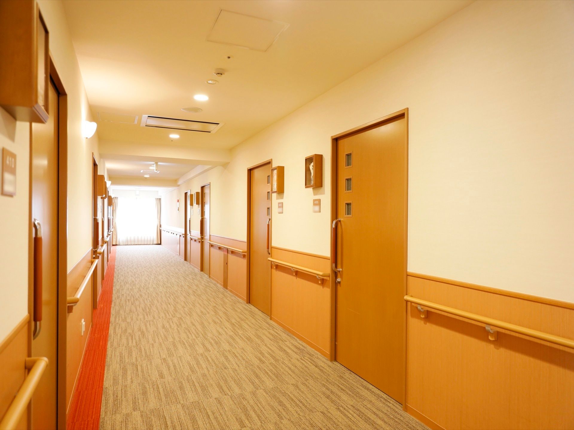 突き当たりの窓から陽光が差し込んでいる明るい通路。両側の壁面に居室の出入口である引き戸が並んでいる。