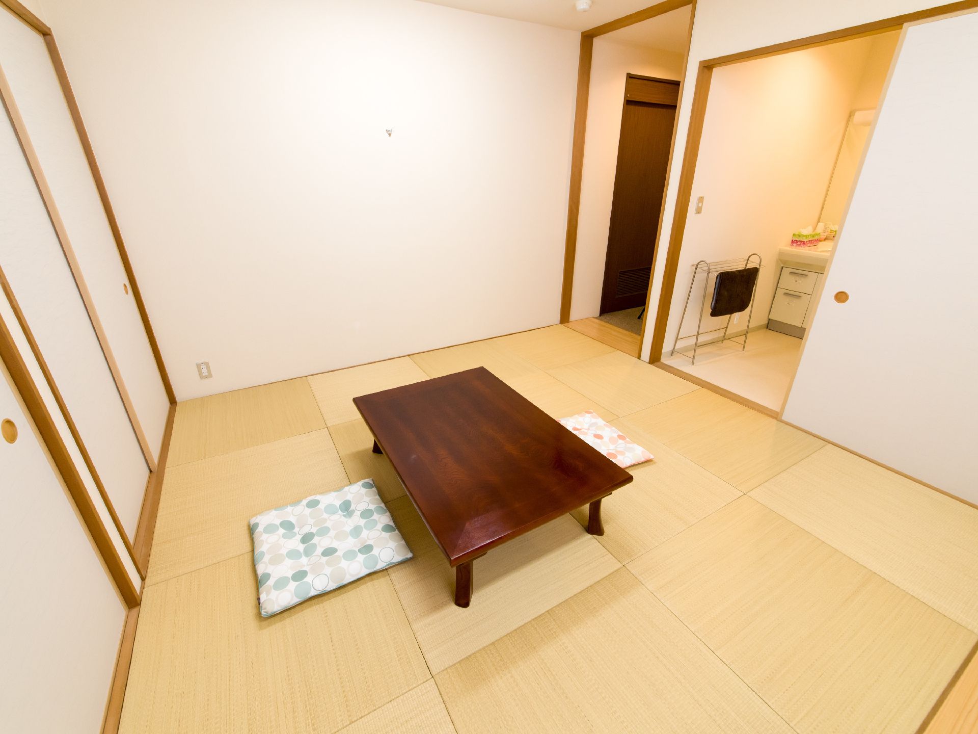 畳が敷かれている和室に、テーブル1台と座布団2枚が用意されている。洗面所、押し入れも設けられている。