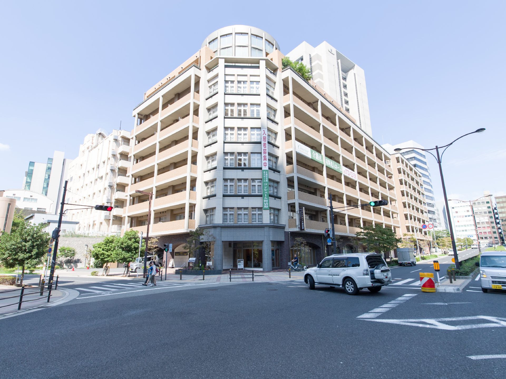 大きな道路の交差点の角地に建っていて、初めての人でもわかりやすい場所にある。下の道路を横断する車や歩行者がみえる。