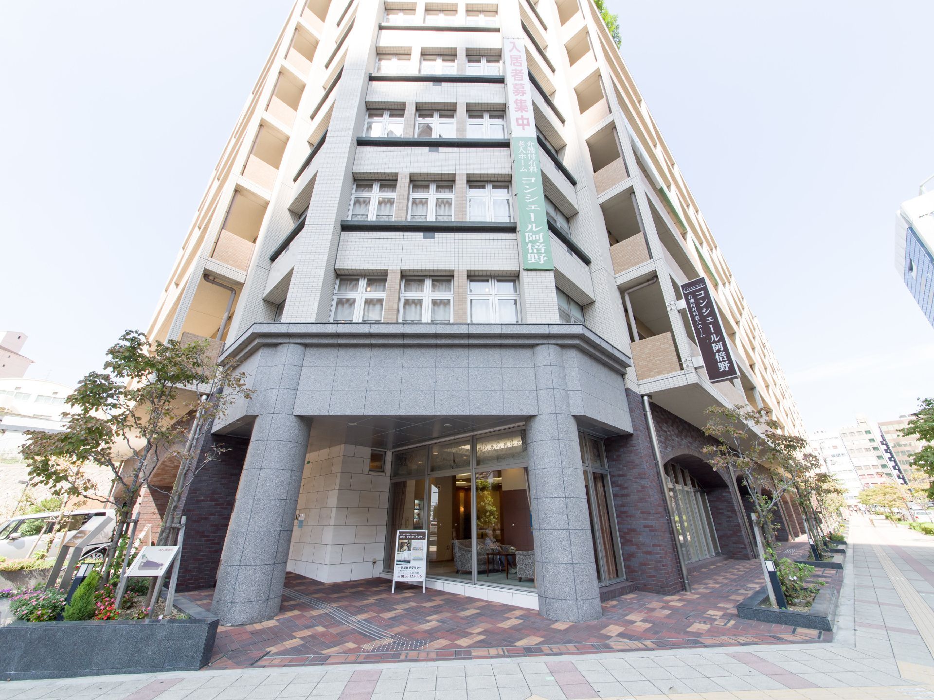 施設は通りの角にあり、とても高い重厚な建物である。入居者様を募集する看板と、施設の種類と名前を書いた看板が出ている。