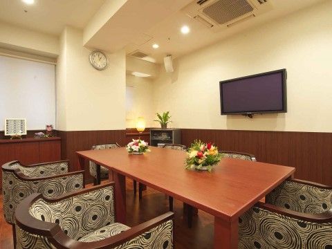 大きなダイニングテーブルを囲んで、１人掛けのデザイン性のあるソファーが複数置かれている。壁にはテレビが設置されている。