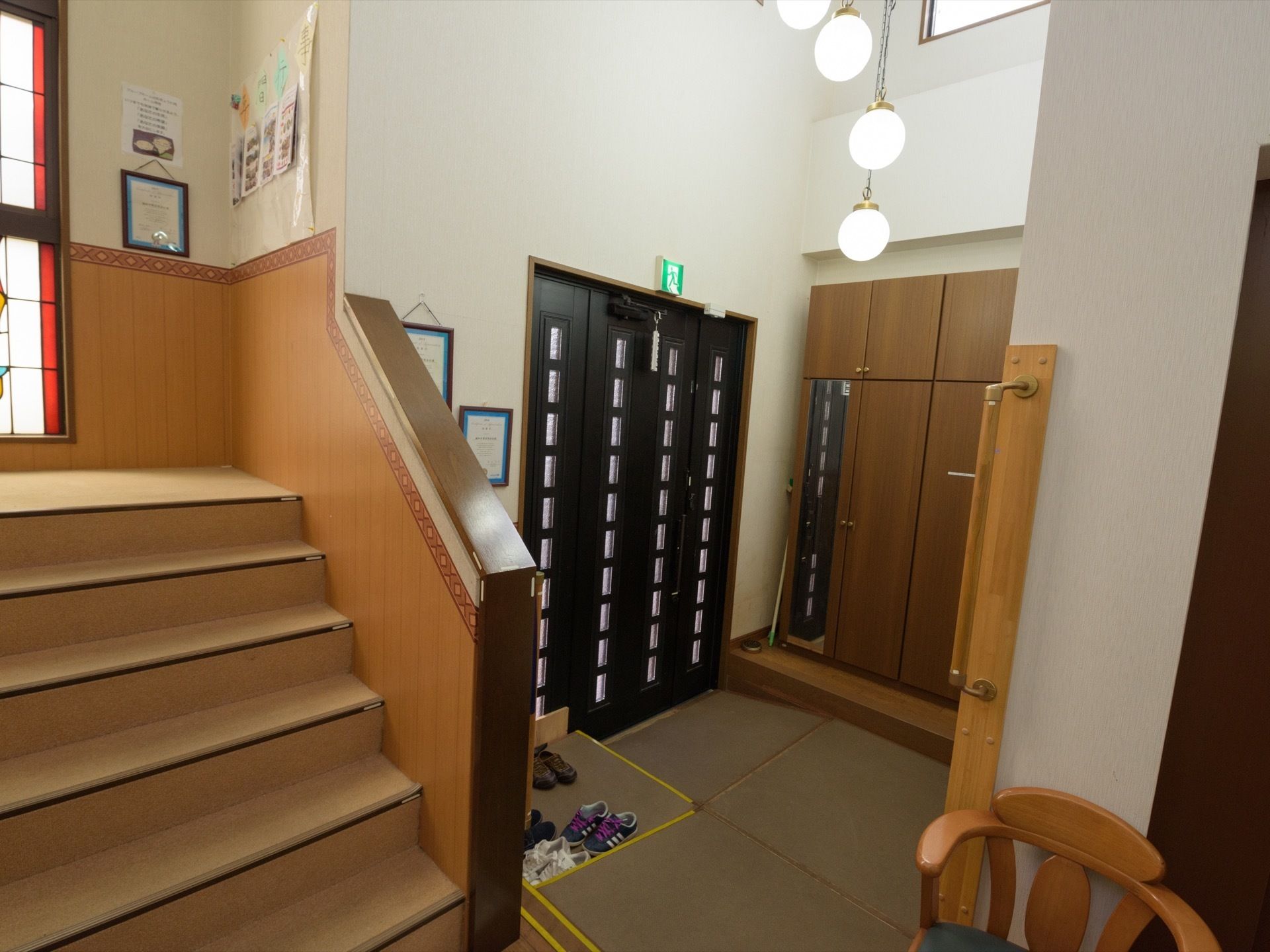 玄関には靴箱が置かれている。縦長の鏡も立てかけられている。扉のすぐは緩やかな斜面がある。上の階へ続く階段もある。