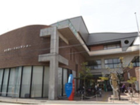 丸型の茶色の屋根とガラス張りの壁面をもつ建物が左手にあり、上部に行政機関の名前が書かれている。１階には駐輪場が設置されている。