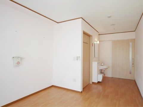 窓を背に居室を見ている。ドアは一部がすりガラスで開口部が大きい引き戸式。引き戸の右側には洗面台が見える。