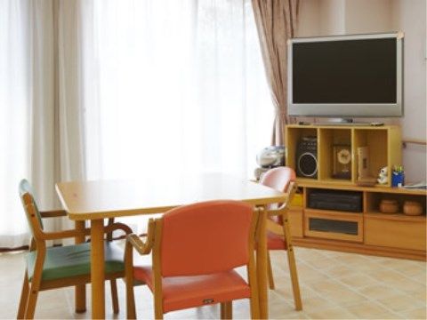 大きな窓がある明るい室内に、ダイニングセットが置かれている。大画面のテレビが載った台があり、囲碁セットも見える。