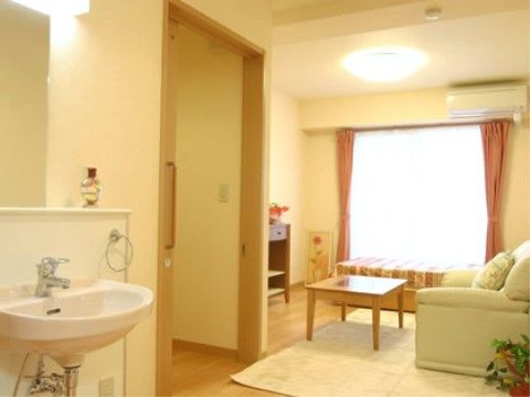 窓際にはベッドが置かれており、テーブル、ソファーも用意されている。観葉植物も飾られている。洗面台もある。