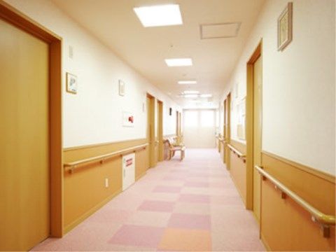通路にはパステルカラーのタイルカーペットが敷かれており、壁側には手すりが取り付けられている。途中で座れるように椅子も用意されている。