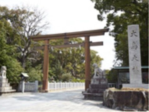 大きな鳥居の右側には神社名が書かれた石像がある。左側には狛犬が置かれている。神社は大きな木に囲まれている。