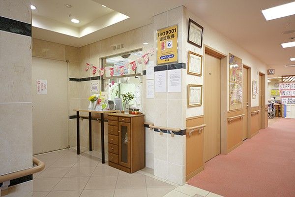 通路の床にはベージュ、ピンク、黄色のタイルカーペットが敷かれており、歩きやすくされている。両側には手すりも設置されている。