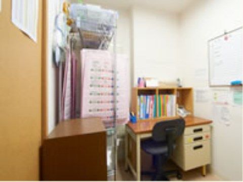 左側の壁にはホワイトボードと、その周りにはメモが多く貼ってある。突き当りには引き出し付きの机があり、その上には書類が立てかけてある。