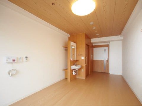 窓から玄関方向に部屋の中を見る。手前左側の壁には非常用ブザーが付いている。玄関扉は引き戸式で縦長の取っ手がある。