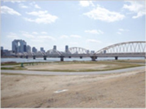 広い河原には、長い橋が架かっている。手前は広い河原になっており、対岸には多くの高いビルが並んでいる。