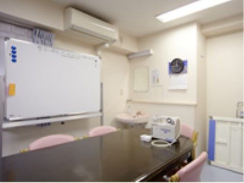 壁には丸い時計、カレンダー、エアコンが付けられている。壁際にはホワイトボードがあり、テーブルや椅子が並べられている。
