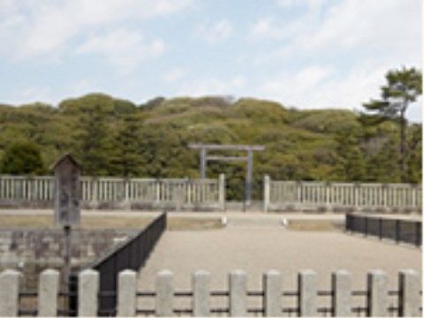 緑豊かな場所に大きな鳥居がある。鳥居の周りは石でできた柵で囲まれている。左側には木の看板が立てかけられている。