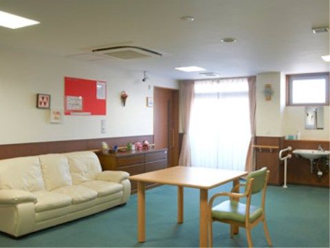 明るい雰囲気の共用リビング。ゆったりとしたソファーや椅子やテーブルが置かれている。壁際には手洗い場も設置されている。