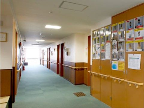 廊下のつき当たりには窓があり、自然光が見えて明るい。両側には居室が並ぶ。壁にはスタッフ紹介の写真が並べて貼られている。