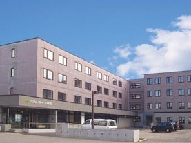 落ち着いたブラウンの壁の4階建ての建物である。グレーの壁に施設名が明記されている。施設内には広い駐車場も完備している。
