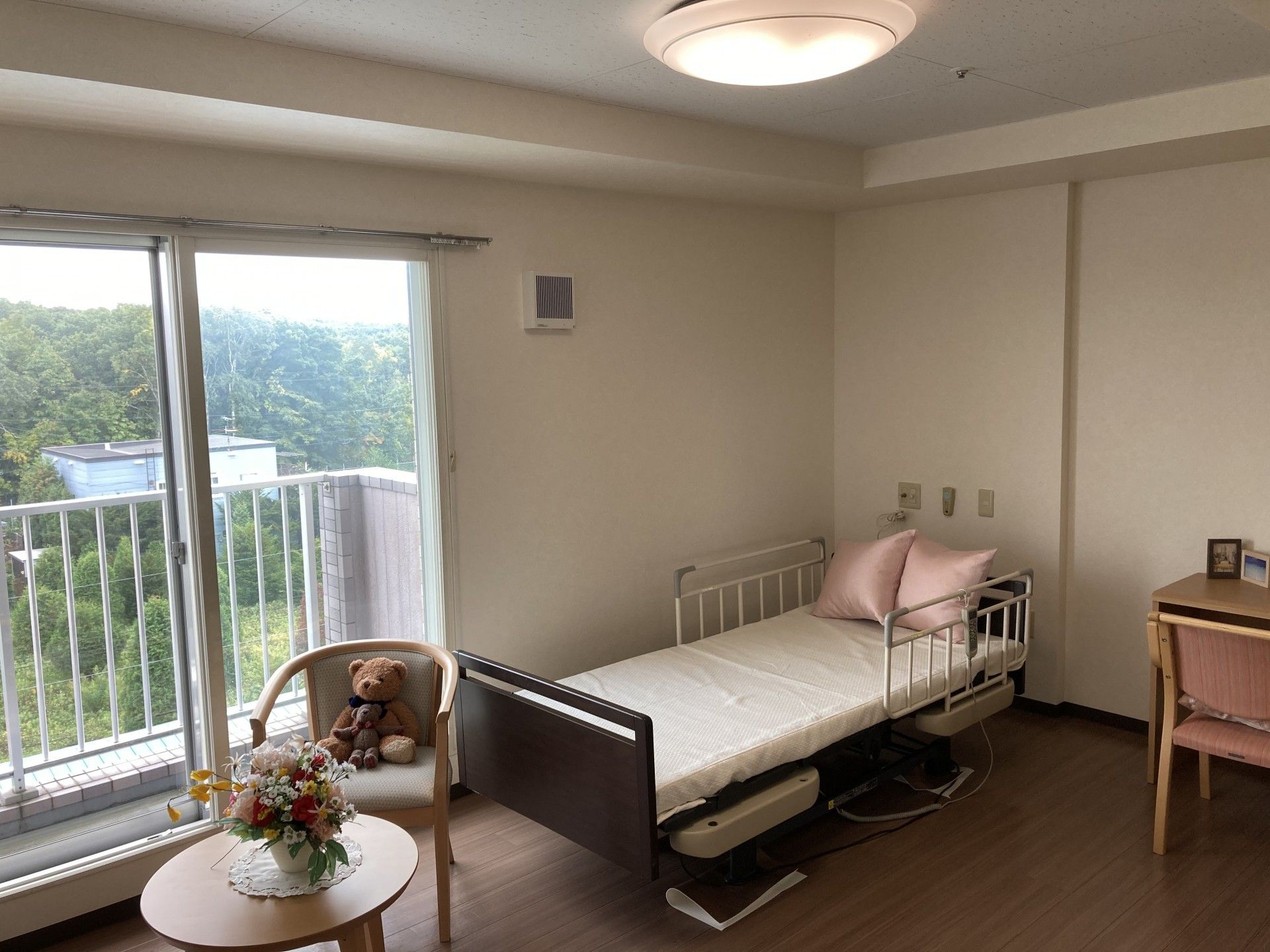 大きな窓のある部屋である。白い壁にブラウンのフローリング。壁には絵が飾られており、洗面台も設置している。