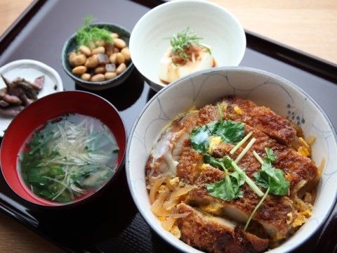 カツ丼やみそ汁、豆の煮ものなどが木製のトレイに乗せられた食事