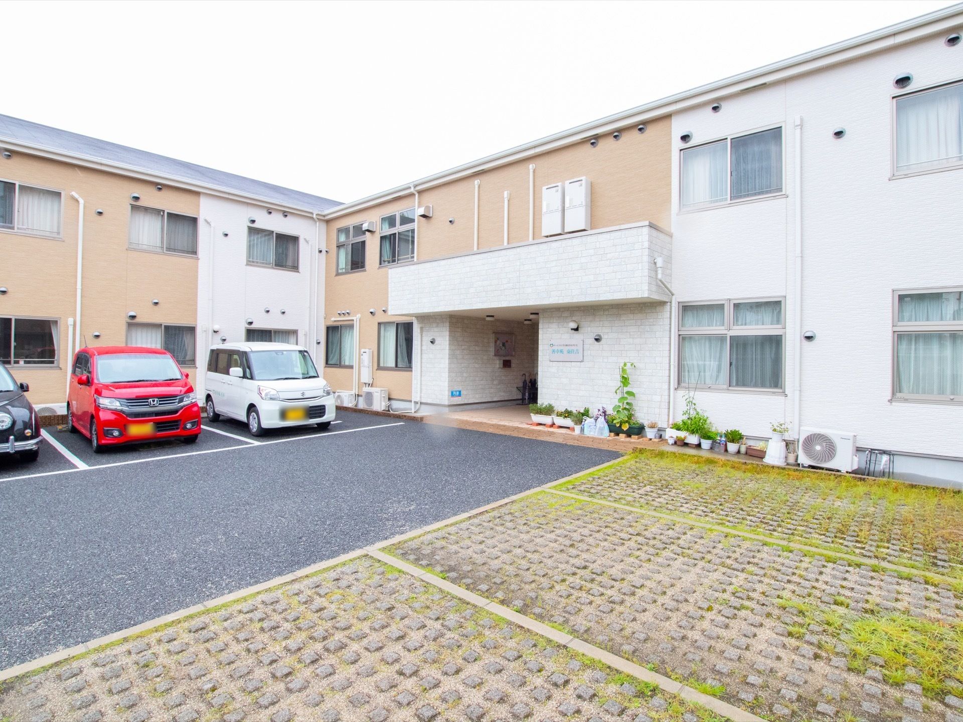 L字型に設計された建物は、ライトブラウンと白のツートンカラーになっている。壁際には、数多くのプランターや植木鉢が並んでいる。