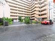 巨大なマンションのような建物である。建物をくぐって向こう側に駐車場が設置されている。木々が敷地内にたくさん植えられている。