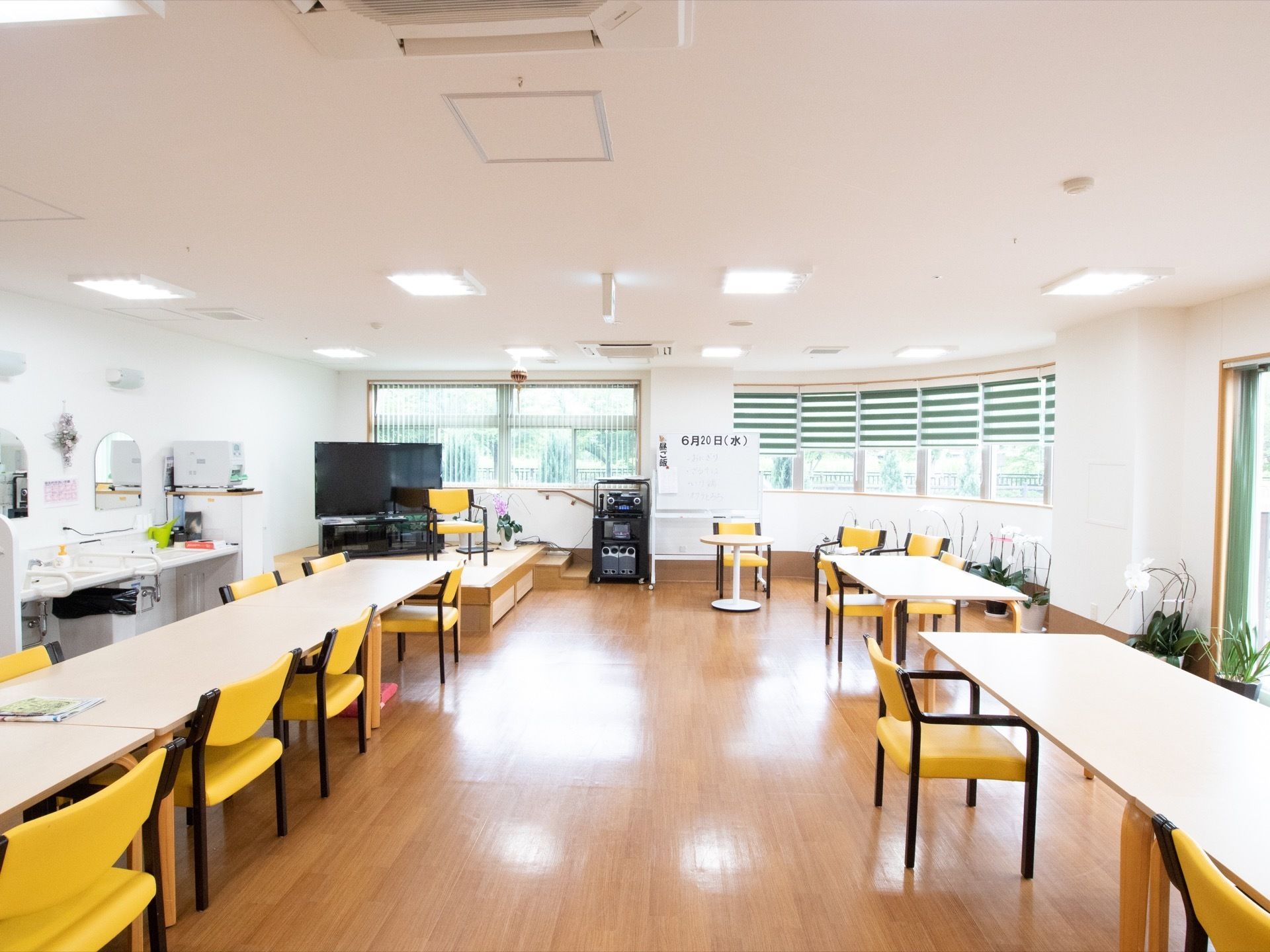 広く明るい共有スペースである。テーブルが並べられており、部屋の隅には洗面台がある。大型のテレビも設置されている。