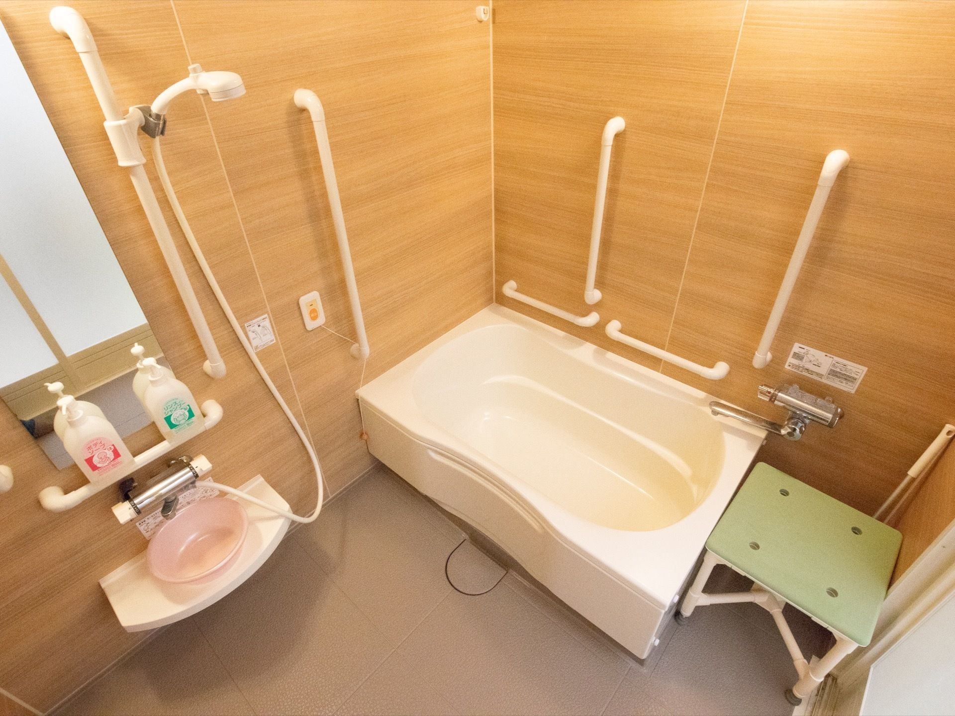 木目調の壁が使われた浴室である。個浴にぴったりの大きさで、浴室の壁には手すりがたくさん備わっている。