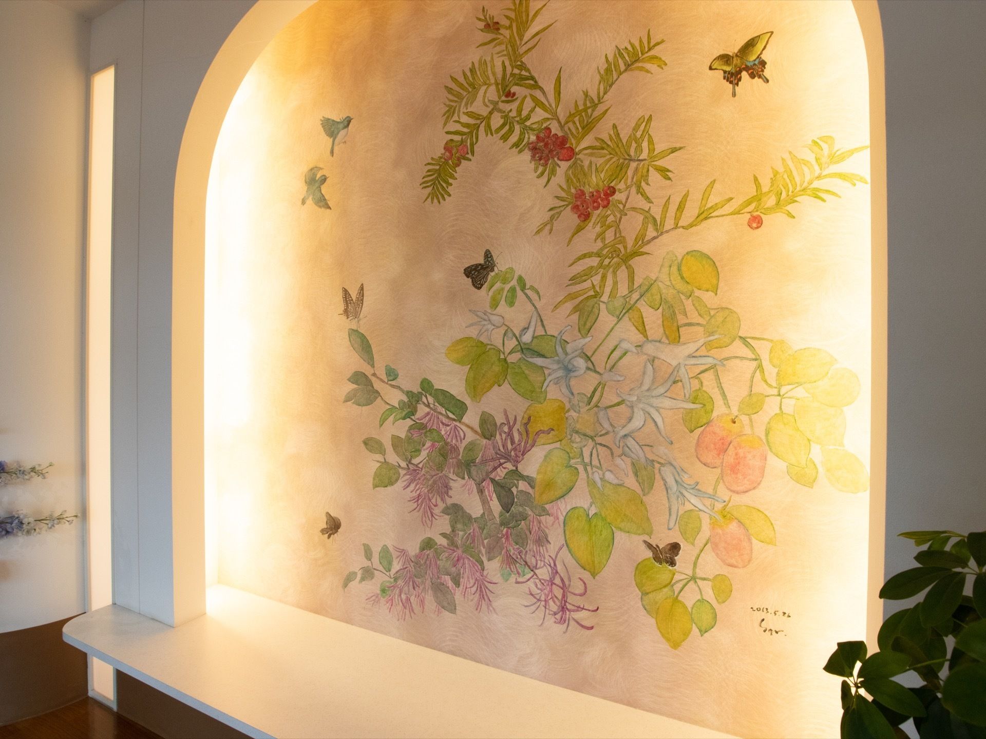 共有スペースにある絵画である。数種類の植物や蝶、鳥が全体に淡いタッチで、壁一面に大きく描かれている。