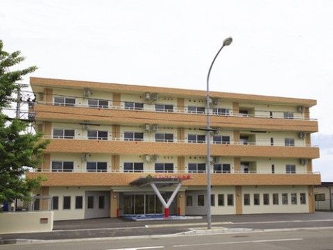 オフホワイトと赤茶色の4階建ての施設には、各居室ごとにベランダを設置している。入口付近には段差がない。