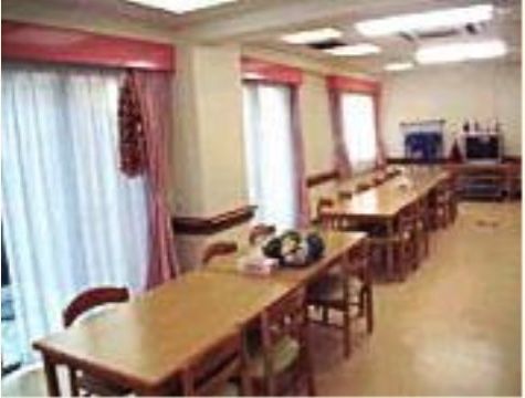 ピンク色のカーテンが掛かった窓際に平行して、長いテーブルが並んでおり、向かい合わせに椅子が並んでいる。突き当りにはテレビが置いてある。