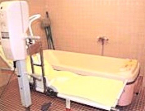 床と壁がタイル貼りの浴室に、特殊介助浴槽が置いてある。傍には電動リフトが付き、横になったまま浴槽に入れる。